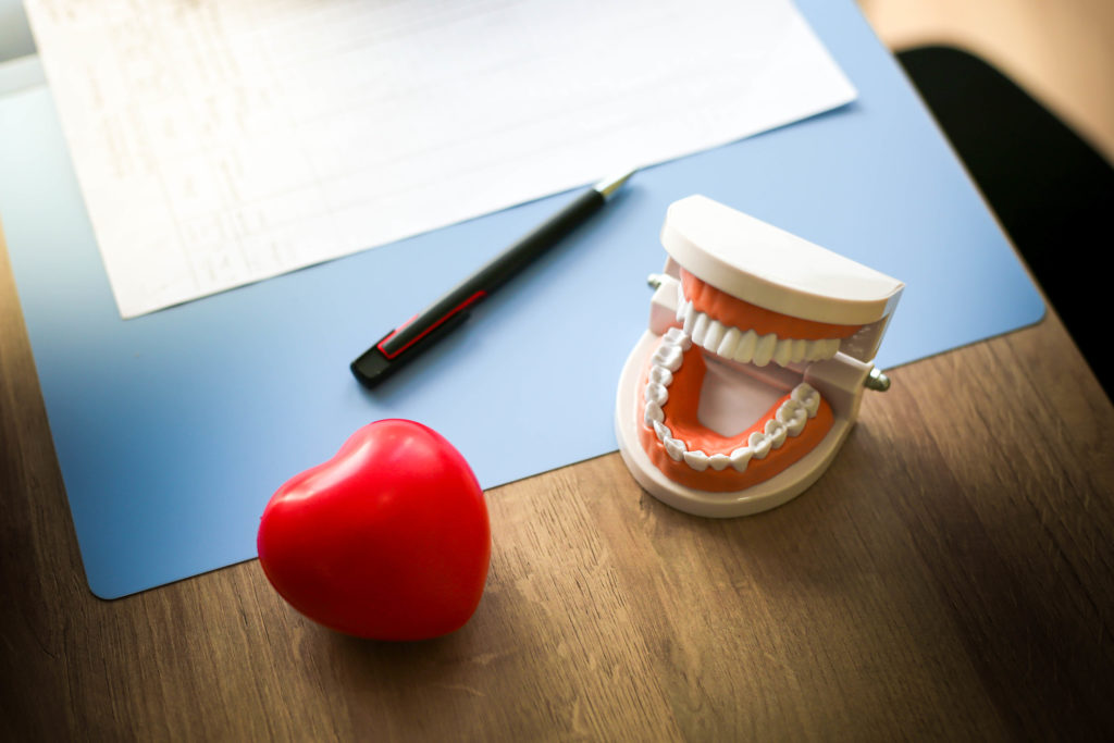 Heart with dental model of teeth on desk with medical chart.