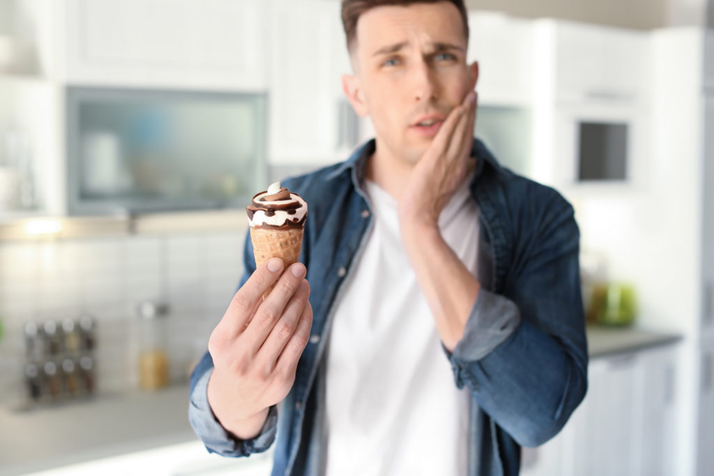 Man eating ice cream holding jaw because of sensitive tooth. Waynesville NC Dentist.